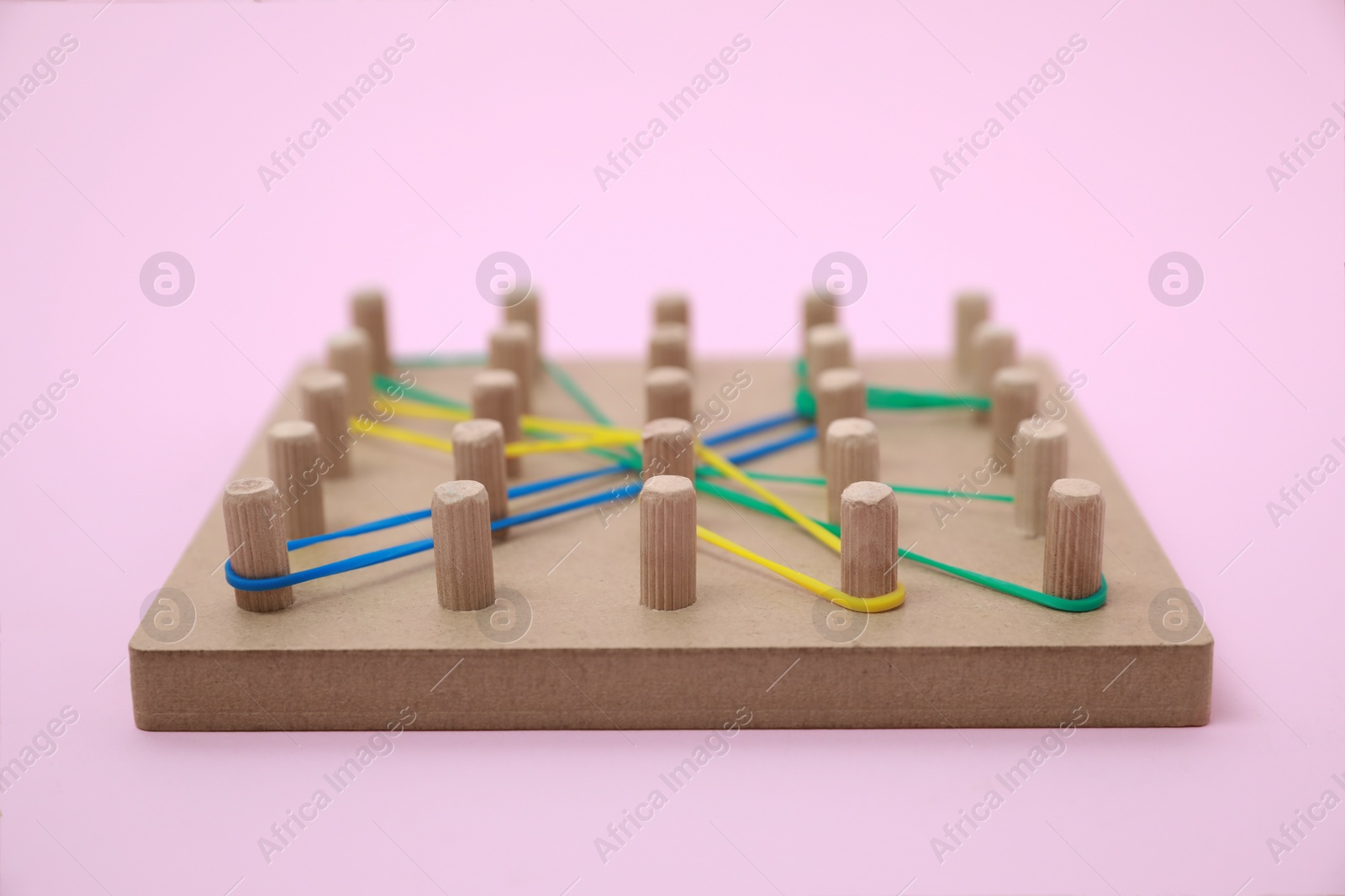 Photo of Wooden geoboard with dragonfly shape made of rubber bands on pink background, closeup. Educational toy for motor skills development