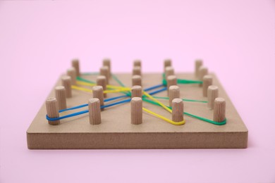 Photo of Wooden geoboard with dragonfly shape made of rubber bands on pink background, closeup. Educational toy for motor skills development