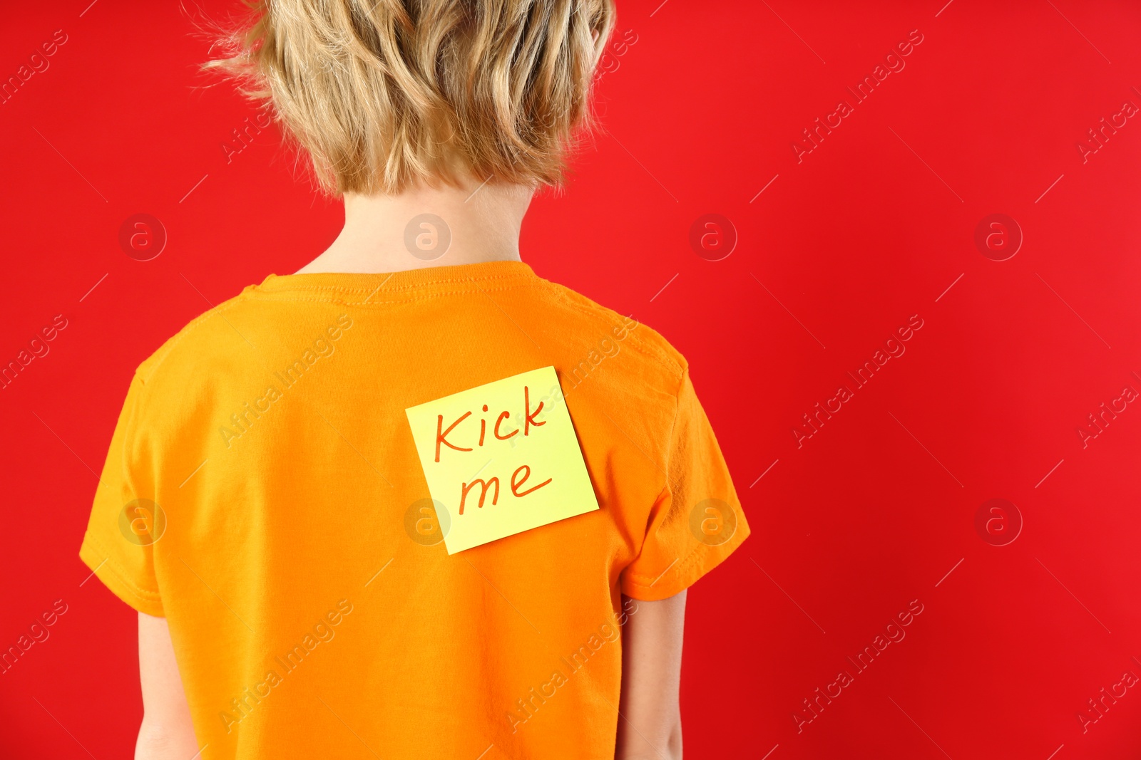 Photo of Little boy with KICK ME sticker on back against red background. April fool's day