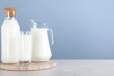Photo of Glassware with fresh milk on grey marble table against light blue background. Space for text