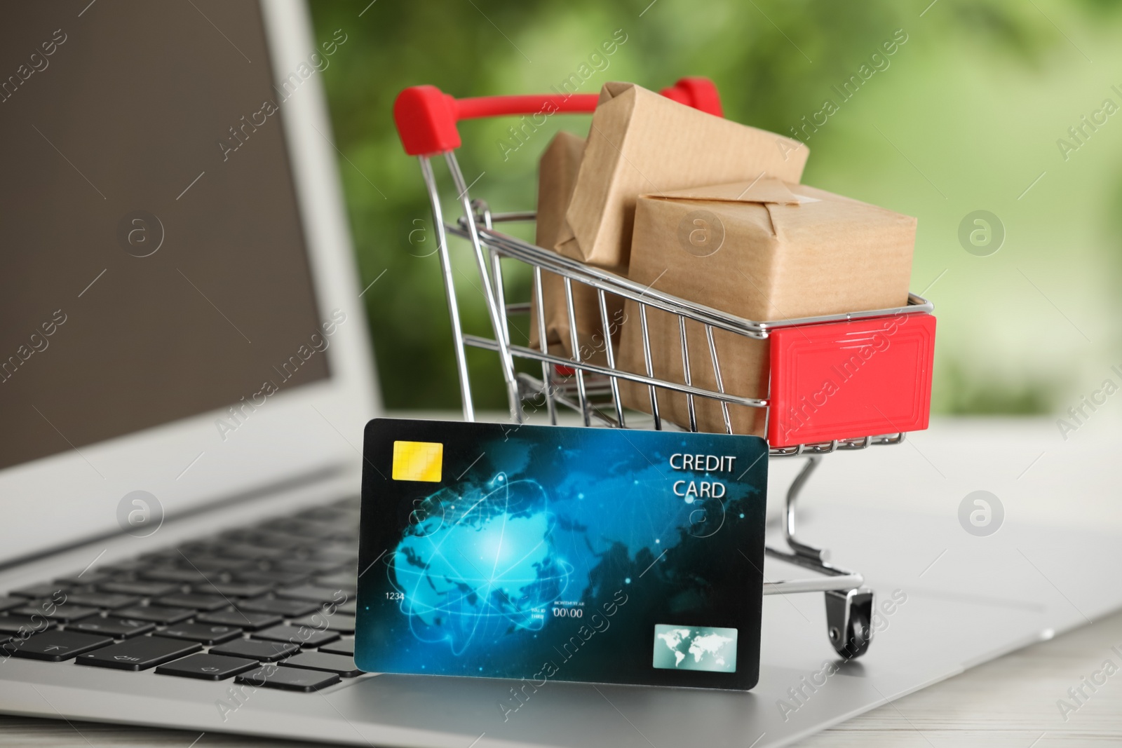 Photo of Online payment concept. Small shopping cart with bank card, boxes on laptop, closeup