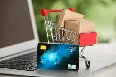 Online payment concept. Small shopping cart with bank card, boxes on laptop, closeup