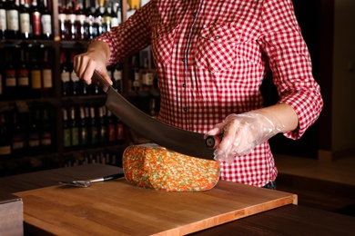 Seller cutting delicious cheese on table in store