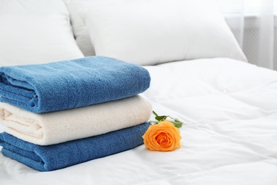 Stack of clean towels and beautiful rose flower on bed. Space for text