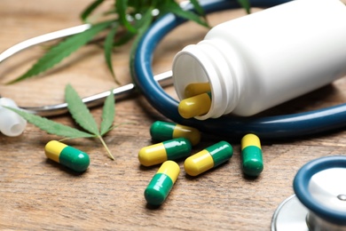 Photo of Hemp leaves, capsules and stethoscope on wooden table, closeup