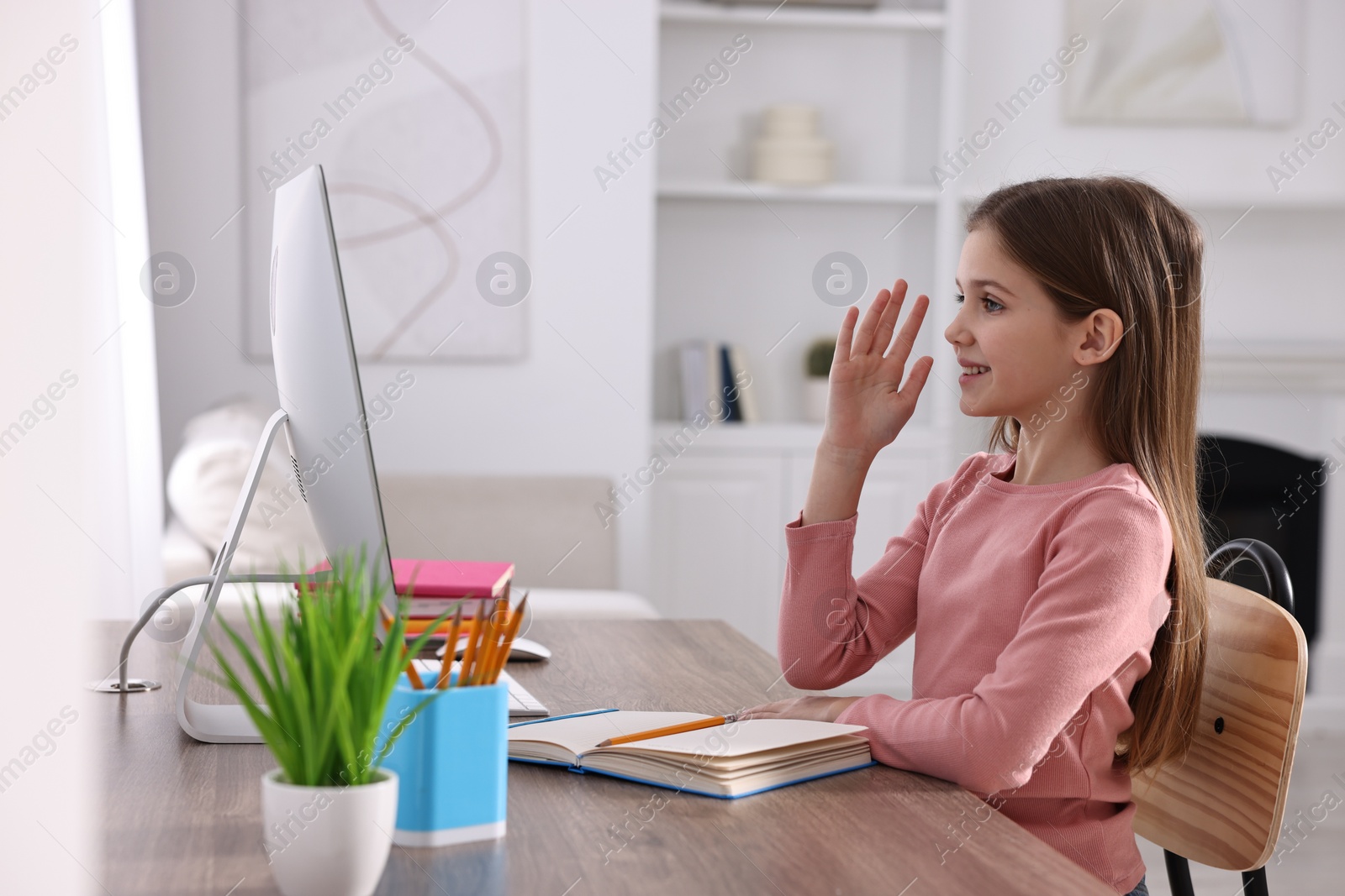 Photo of E-learning. Cute girl raising her hand to answer during online lesson at table indoors