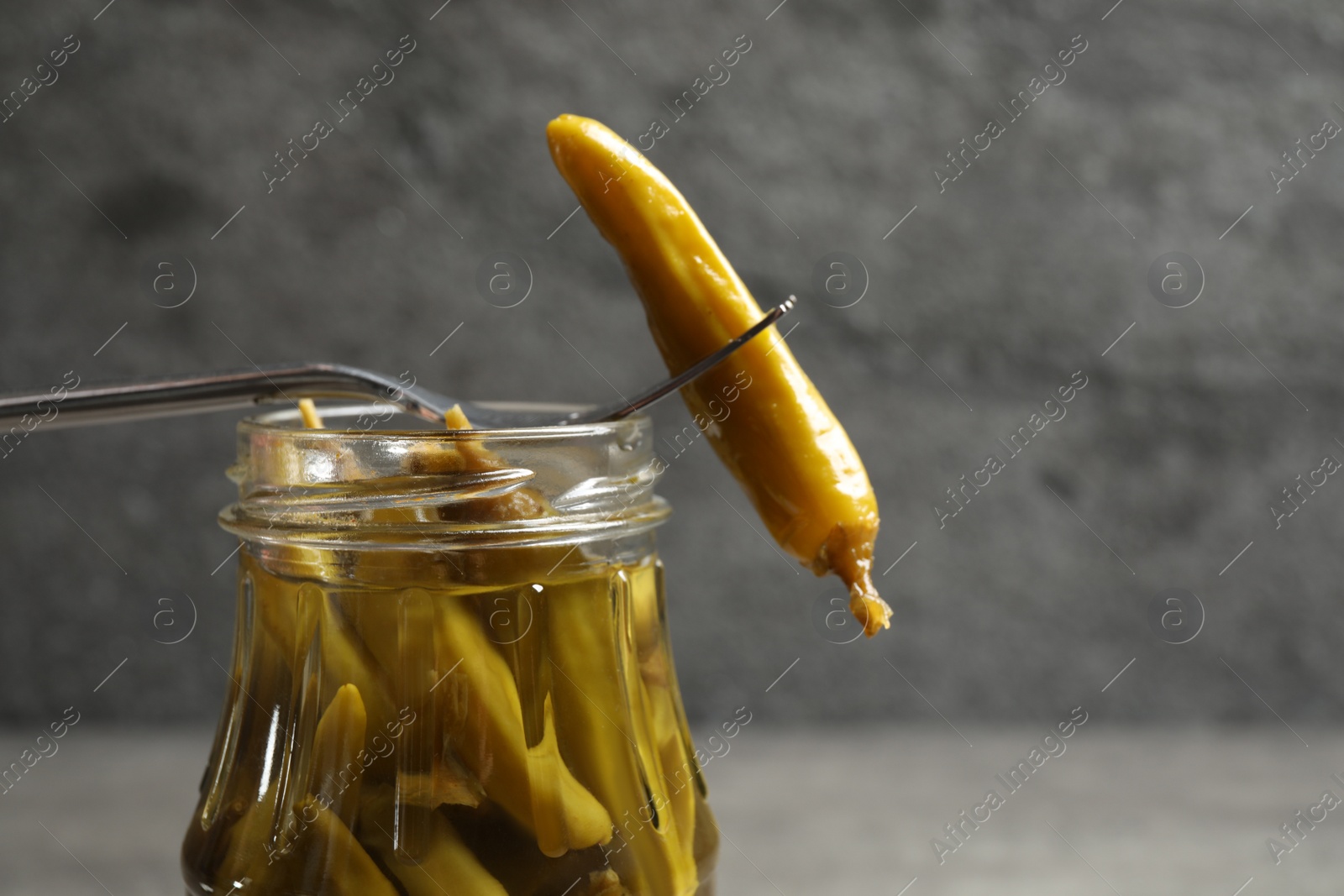 Photo of Fork with pickled pepper and jar on grey table, closeup