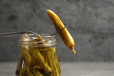 Fork with pickled pepper and jar on grey table, closeup