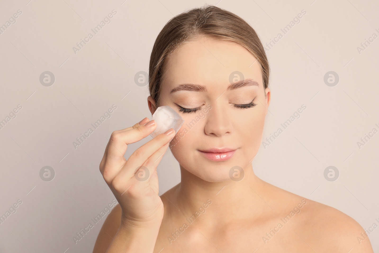 Photo of Young woman with ice cube on light background. Skin care