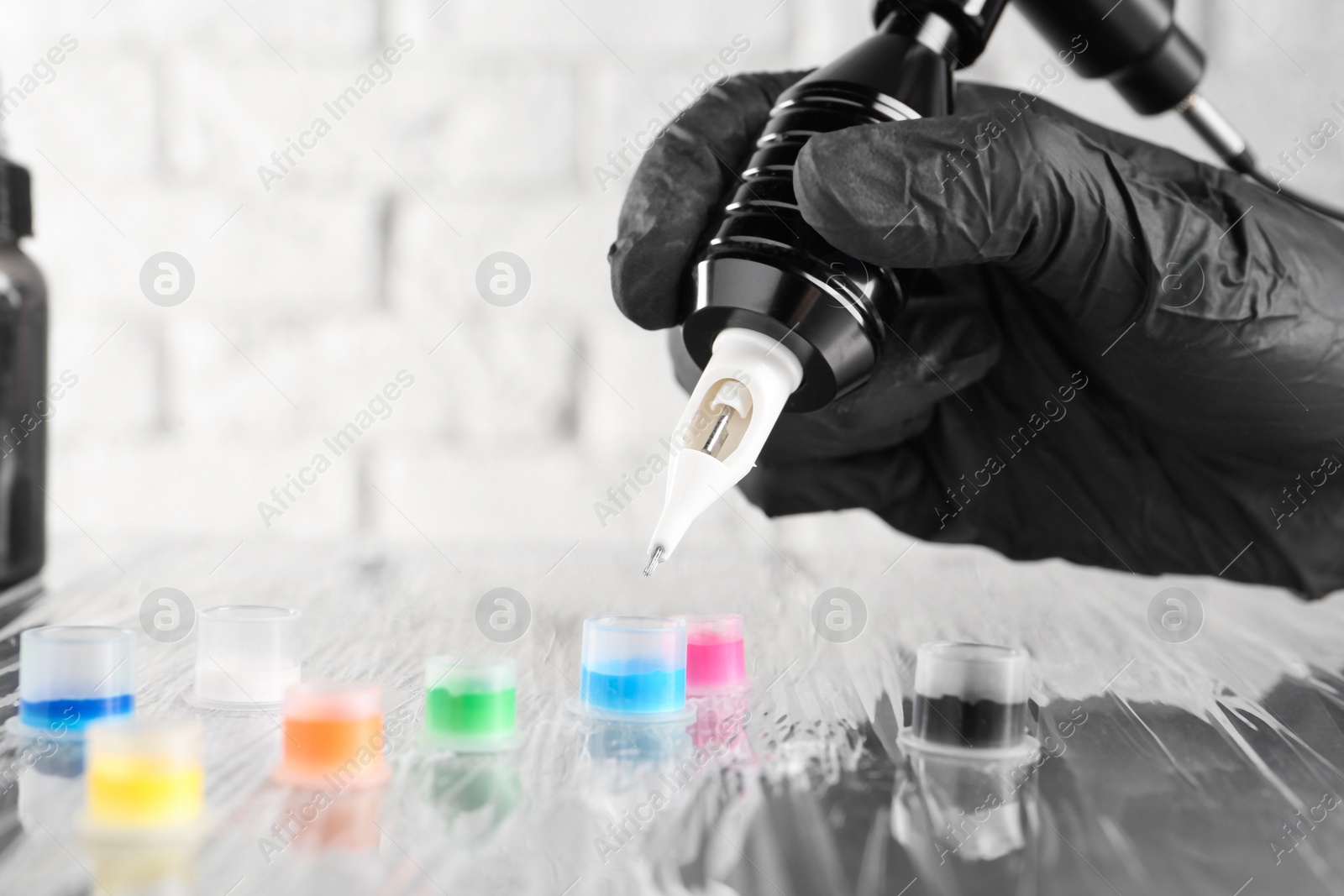 Photo of Tattoo artist with professional machine and colorful inks at table, closeup