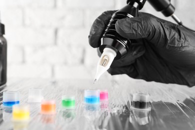 Photo of Tattoo artist with professional machine and colorful inks at table, closeup