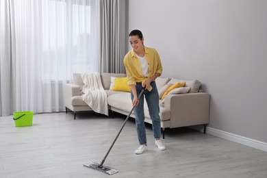 Young woman cleaning floor with mop in living room