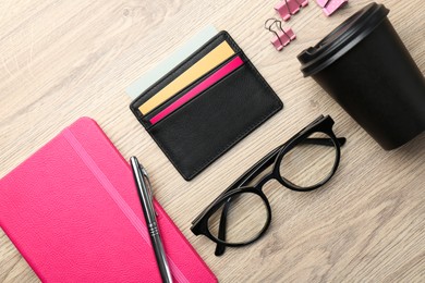 Leather business card holder with colorful cards, stationery, glasses and coffee on wooden table, flat lay