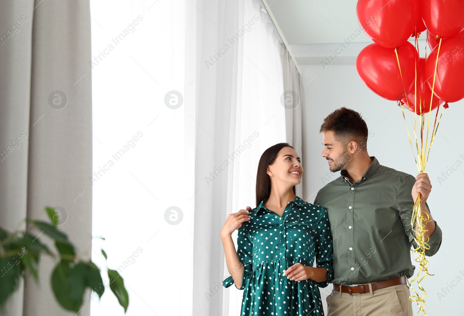 Photo of Young couple with air balloons at home. Celebration of Saint Valentine's Day