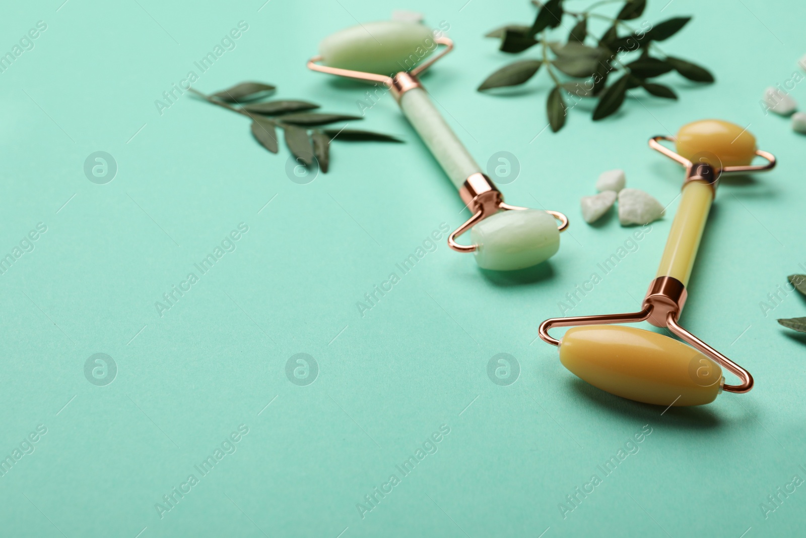 Photo of Natural face rollers and leaves on turquoise background. Space for text