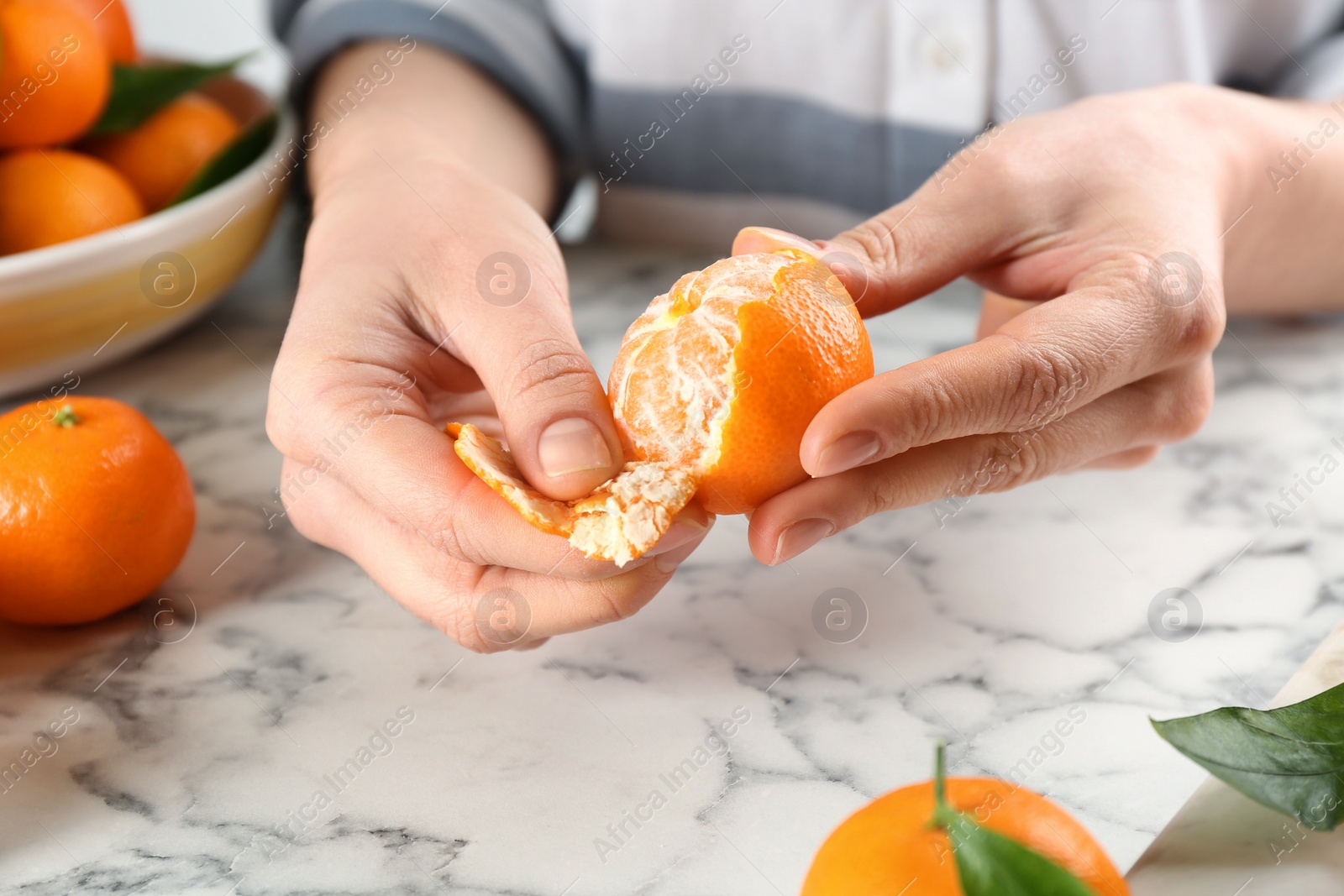 Photo of Woman peeling fresh ripe tangerine at white marble table, closeup