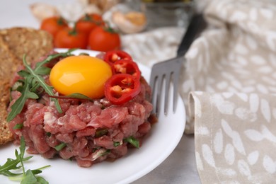 Photo of Tasty beef steak tartare served with yolk, pepper, sliced bread and greens on white table, closeup