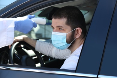 Photo of Doctor measuring driver's temperature with non contact infrared thermometer outdoors