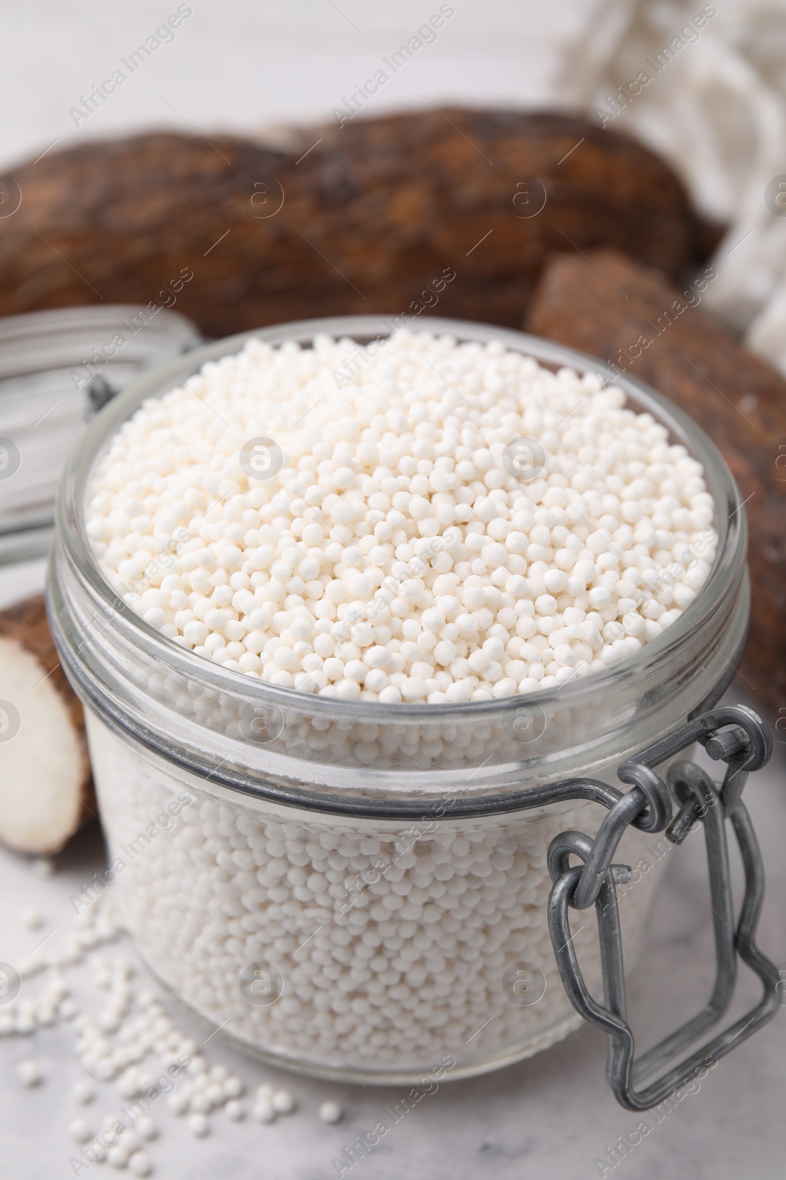 Photo of Tapioca pearls in jar and cassava roots on white table, closeup