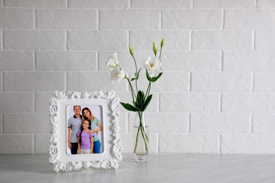 Framed family photo near beautiful bouquet on white table