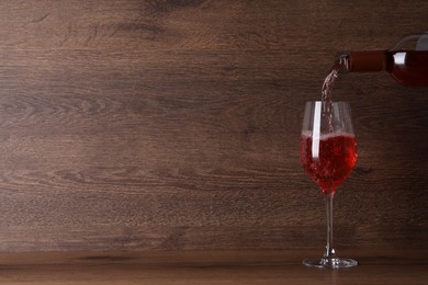 Photo of Pouring delicious rose wine into glass on table against wooden background. Space for text