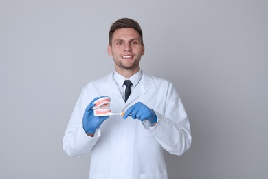 Photo of Dentist with jaws model and toothbrush on light grey background. Oral care demonstration