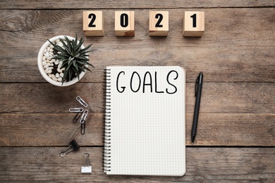 Photo of Notebook with word Goals near number 2021 made of cubes, new year aims. Objects on wooden table, flat lay