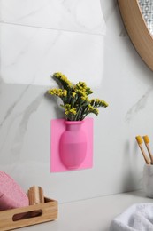 Photo of Silicone vase with flowers on white marble wall over countertop in stylish bathroom
