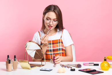 Beauty blogger applying lipgloss at table on pink background