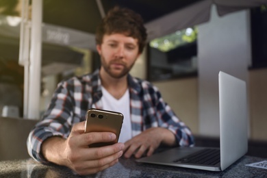 Photo of Handsome man using smartphone at table in cafe, focus on hand