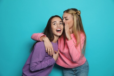 Photo of Young woman laughing while her friend whispering something funny against color background