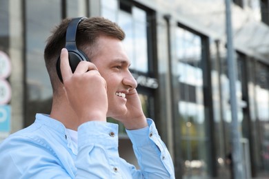 Man wearing headphones near building outdoors. Space for text
