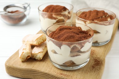Photo of Delicious tiramisu in glasses and cookies on white table
