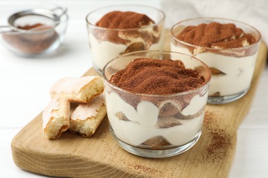 Delicious tiramisu in glasses and cookies on white table