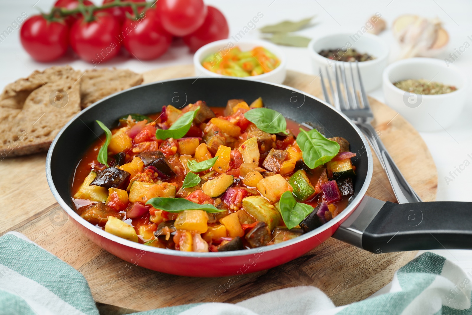 Photo of Frying pan with tasty ratatouille on wooden board