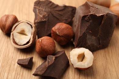 Photo of Delicious chocolate chunks and hazelnuts on wooden table, closeup