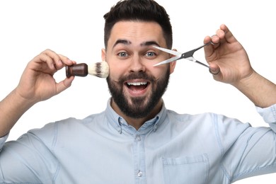 Photo of Handsome young man with mustache holding scissors and shaving brush on white background