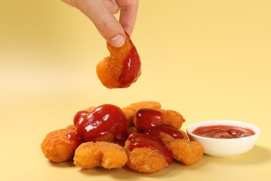 Photo of Woman holding delicious chicken nugget with ketchup on pale yellow background, closeup