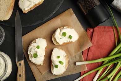 Photo of Bread with cream cheese and green onion on black table, flat lay