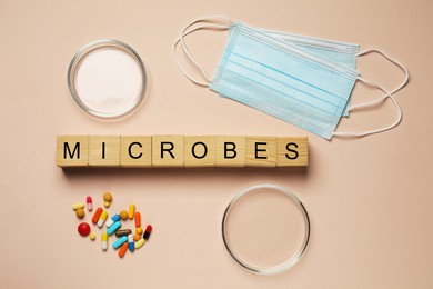 Word Microbes made with wooden cubes, colorful pills, Petri dishes and face masks on beige background, flat lay