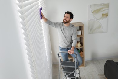 Smiling man on metal ladder wiping blinds at home, above view