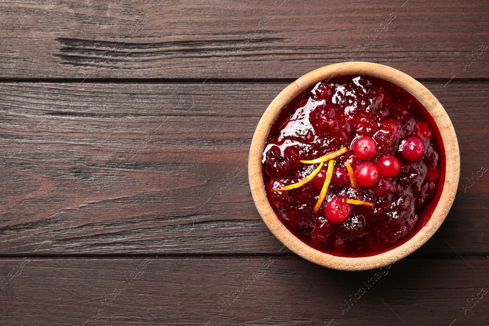 Photo of Cranberry sauce with orange peel on wooden table, top view. Space for text