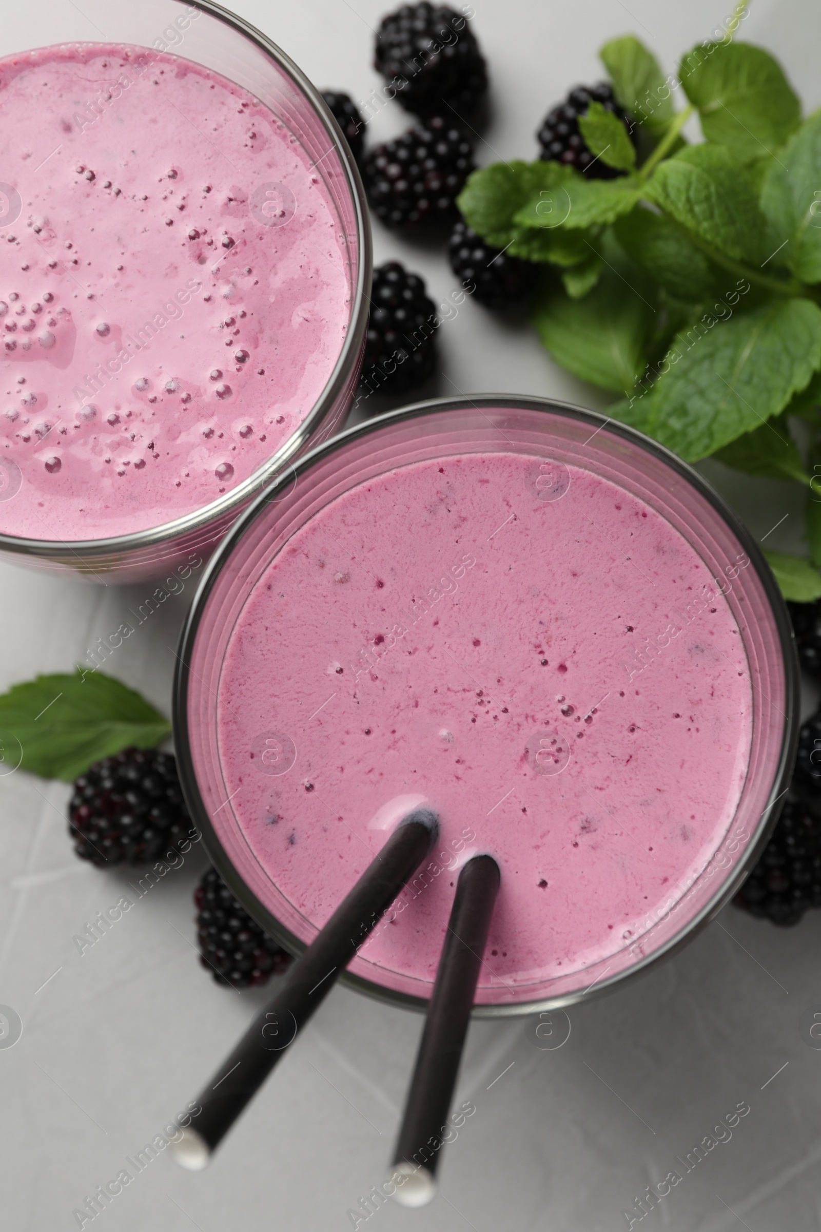 Photo of Delicious blackberry smoothie in glasses, fresh berries and mint on grey table, flat lay