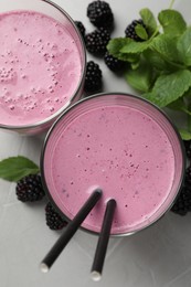 Delicious blackberry smoothie in glasses, fresh berries and mint on grey table, flat lay