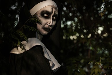 Photo of Portrait of scary devilish nun near tree outdoors, space for text. Halloween party look
