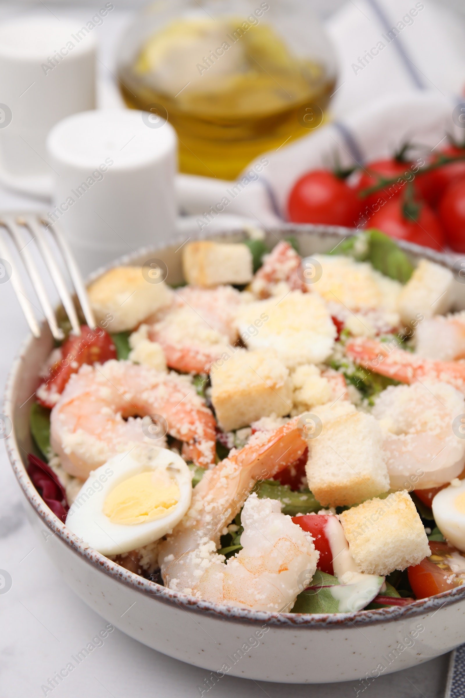 Photo of Delicious Caesar salad with shrimps served on white marble table, closeup