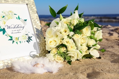 Photo of Composition with wedding invitation and gold rings on sandy beach