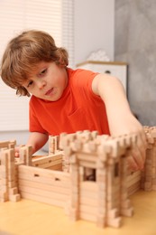 Cute little boy playing with wooden construction set at table in room. Child's toy