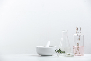 Photo of Ingredients for herbal cosmetic products and  laboratory glassware on white table. Space for text