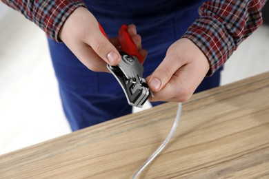 Professional electrician stripping wiring at wooden table, closeup view